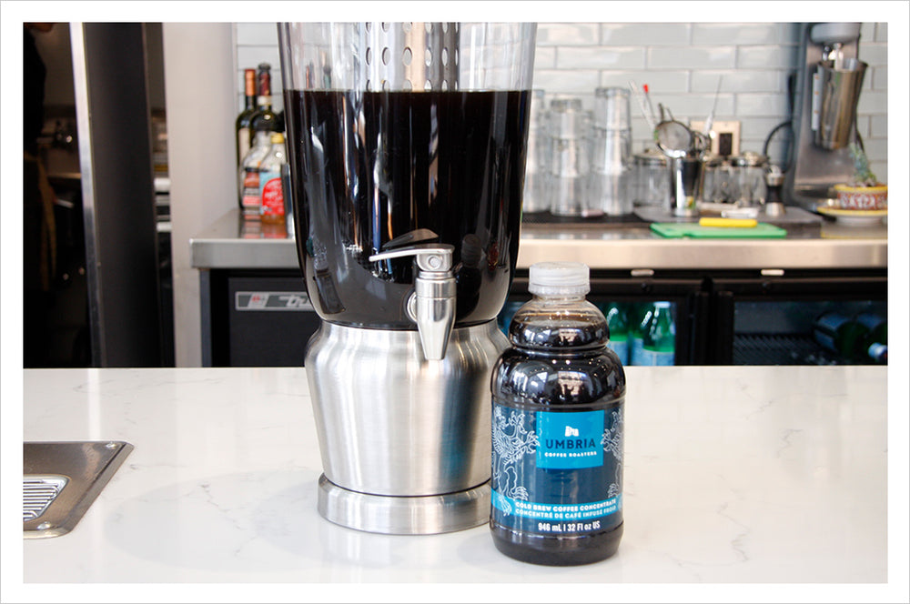 a bottle of umbria cold brew concentrate in front of a dispenser filled with cold brew