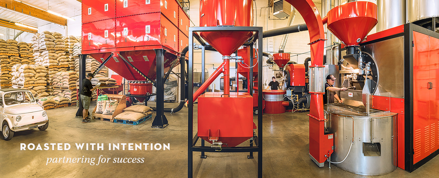 Red coffee roasting machinery in a warehouse setting with text 'Roasted with Intention'.