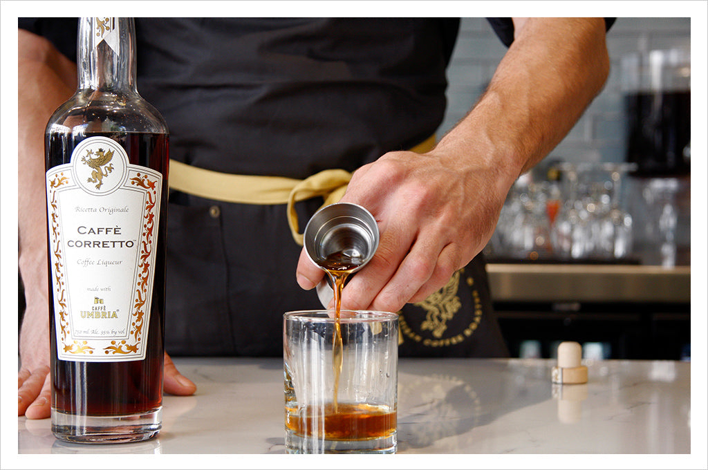 a man pours caffe corretto into a glass, next to a bottle of caffe corretto