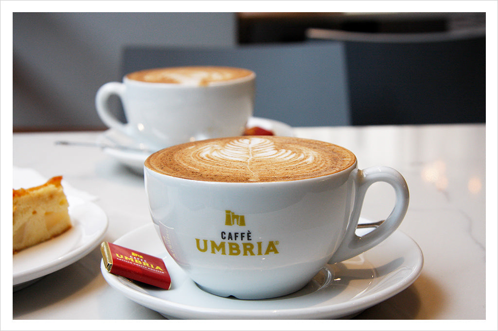 a coffee with latte art in a logo cup with a pastry next to it and other coffee in background