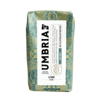 A 12 oz bag of Umbria Coffee Roasters Leone Blend light roast coffee, featuring a green and gold patterned bag with a white label.
