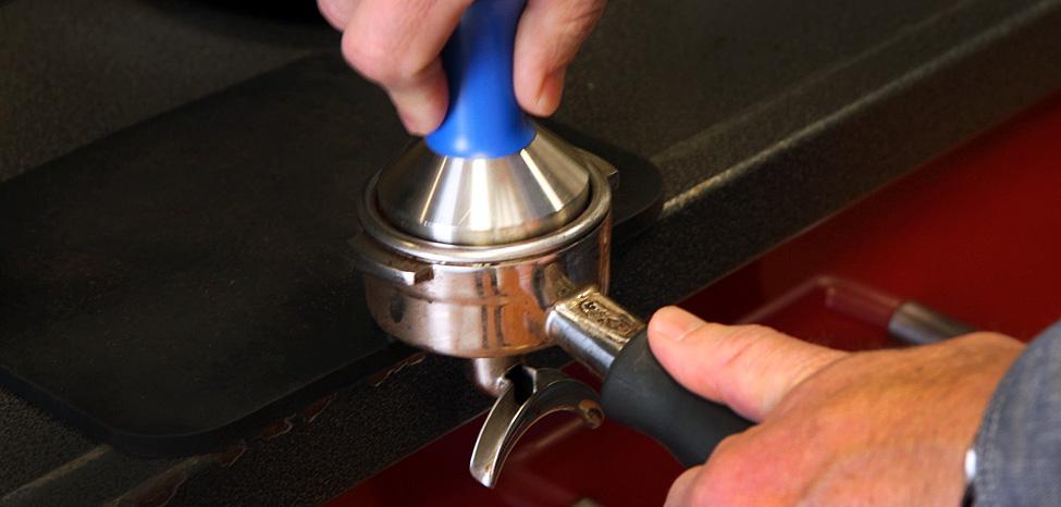 a person tamping coffee grounds in portafilter
