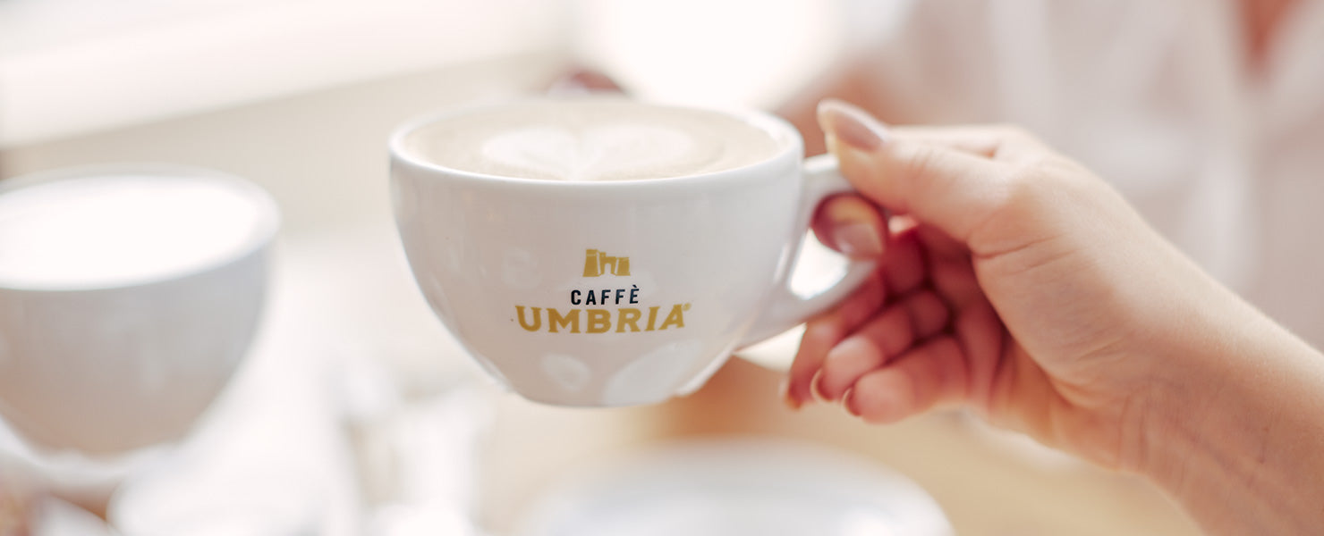 Hand holding a cup of coffee with 'Caffè Umbria' text, blurred background
