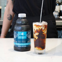 coffee concentrate bottle, glass of cold brew coffee with milk pouring in
