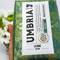 A hand hold a green leone blend bag, flowers in background